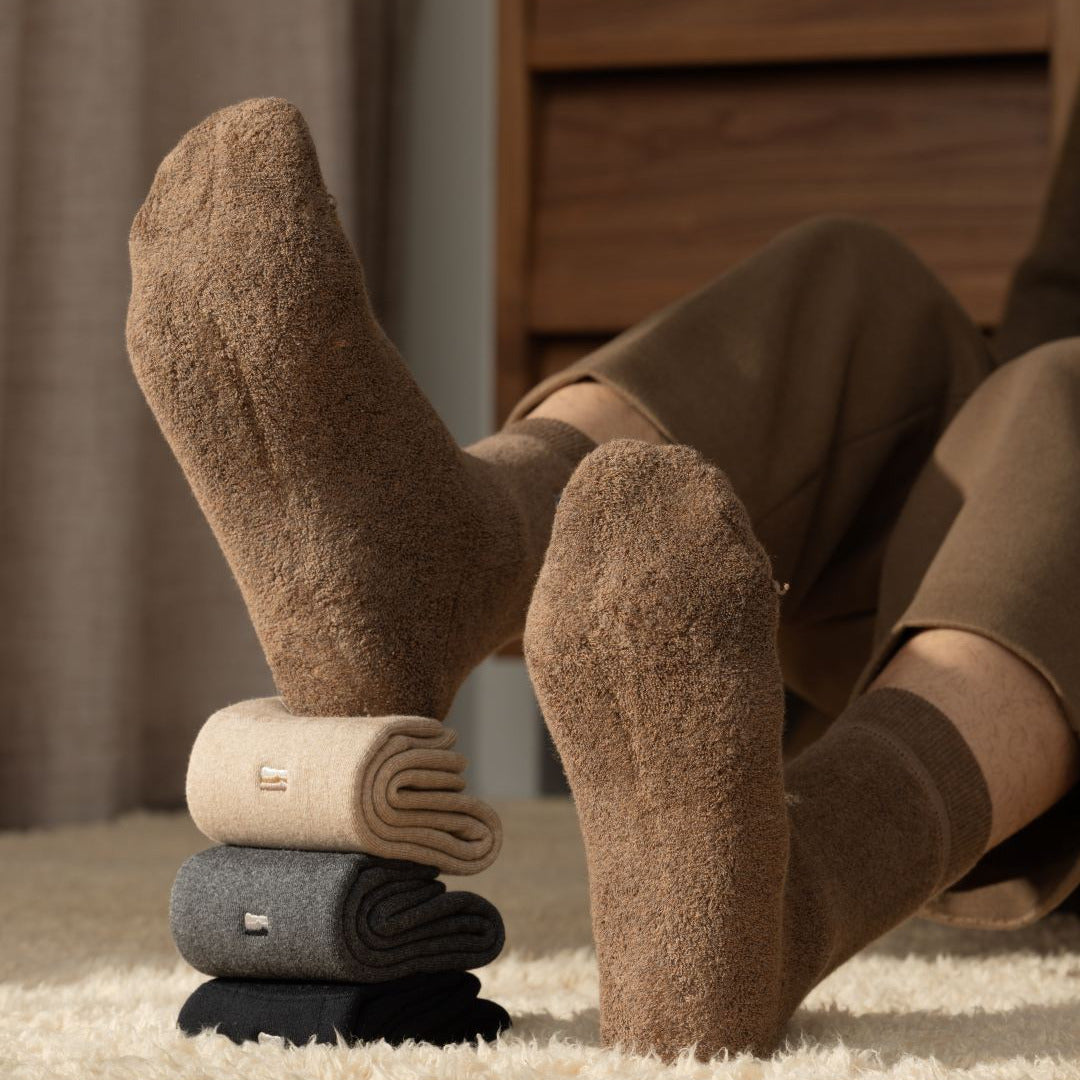 Brown socks being worn with a stack of folded socks on a carpeted floor.