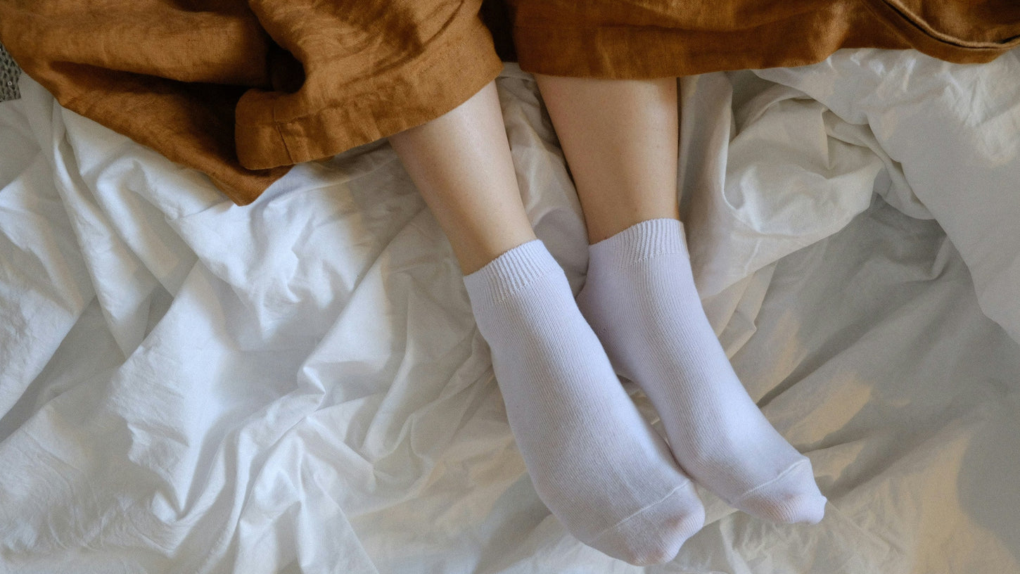 Person wearing white socks on a bed with brown pants.
